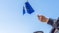 Ein Mann hält eine kleine Europaflagge aus dem Autofenster.