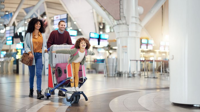 Eine Familie wartet am Flughafen-Terminal mit Gepäckwagen auf den Check-in.