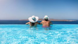 Paar mit Sonnenhüten genießt den Sommerurlaub in einem Infinity Pool mit Aussicht auf das Meer.