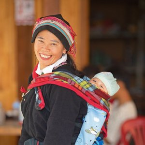 Frau in traditioneller Dao-Tracht trägt ein Baby auf ihrem Rücken.