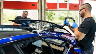 Zwei Männer setzen eine Windschutzscheibe in ein Auto ein. 