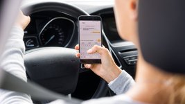 Eine Autofahrerin hält ihr Smartphone während der Autofahrt in der Hand.