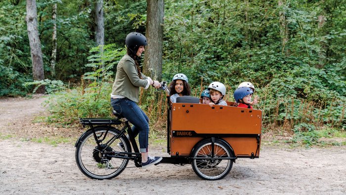 Ein Lastenfahrrad mit Platz für bis zu sechs Kinder auf einem Waldweg unterwegs.