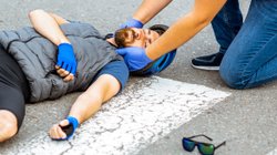 Ersthelfer versorgt verletzten Radfahrer nach Verkehrsunfall. 