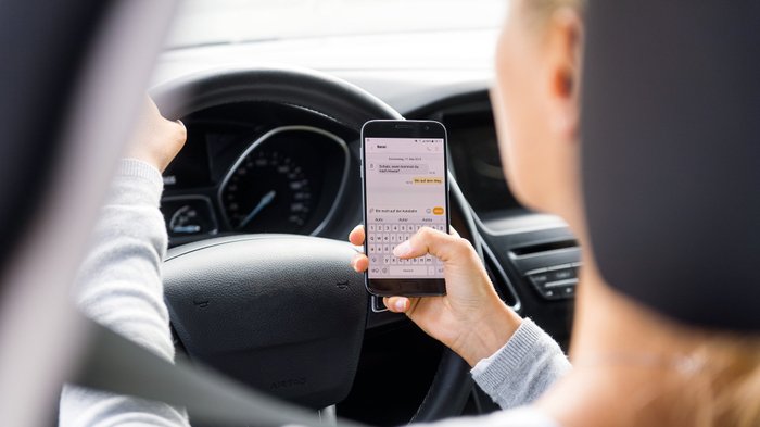 Eine Autofahrerin hält ihr Smartphone während der Autofahrt in der Hand.