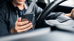 Mann benutzt ein Smartphone während der Fahrt im Auto und ist vom Verkehrsgeschehen abgelenkt.