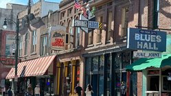 Belebte Straße mit Leuchtreklamen von Musikclubs und Restaurants.