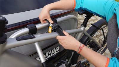 Frau hält Befestigung eines Fahrradträgers in der Hand. 