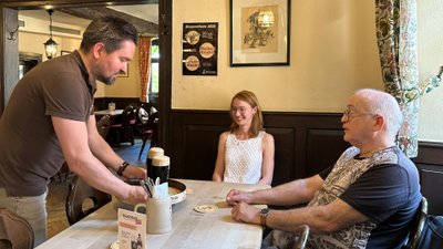 Kellner bringt Brauerei-Gästen zwei Gläser Bier zu ihrem Tisch.