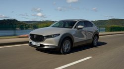 Ein Mazda CX-30 fährt bei Sonnenschein auf einer Straße 
