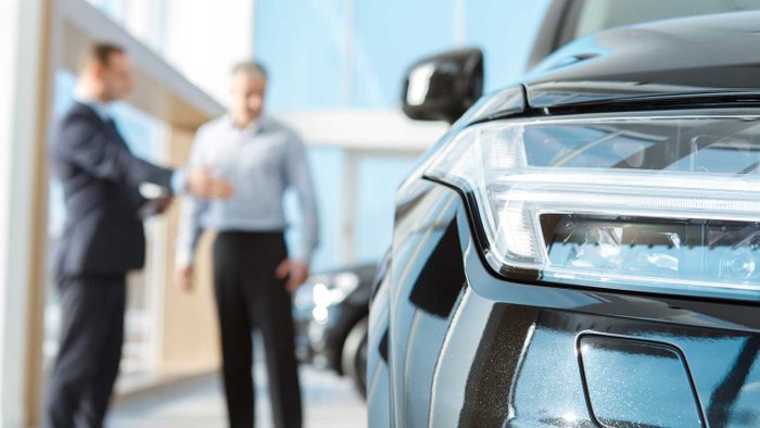 Autoverkäufer und Kunde stehen vor einem Neuwagen.