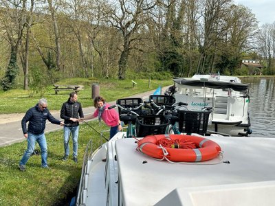 Drei Personen vertäuen ein Hausboot am Ufer eines Flusses.