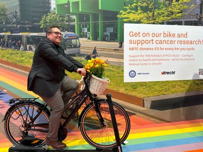 Mann radelt auf einem Fahrrad mit Korb und Blumenstrauß vor buntem Hintergrund.