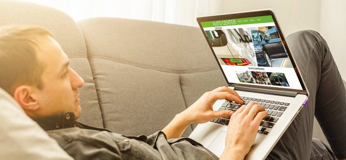 Mann sucht auf dem Laptop am Sofa nach Autos.