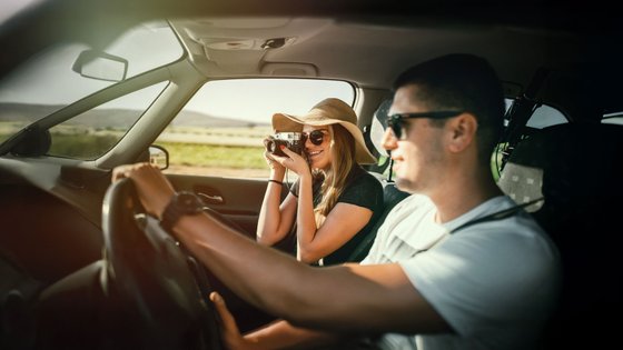 Paar sitzt in einem Auto und die Beifahrerin fotografiert.