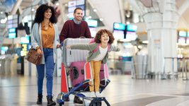 Eine Familie wartet am Flughafen-Terminal mit Gepäckwagen auf den Check-in.