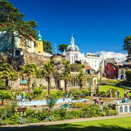 Park mit bunten Blumen und Wasserfläche, dahinter bunte Häuserfassaden und Kirchtürme.