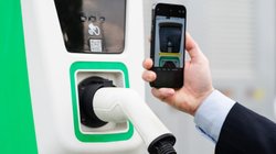 Ein Mann scannt den QR-Code an einer Ladesäule mit seinem Smartphone.. 