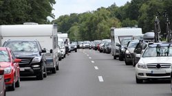 Autos und Wohnwagen stehen bei der Fahrt in den Urlaub auf einer Autobahn im Stau.