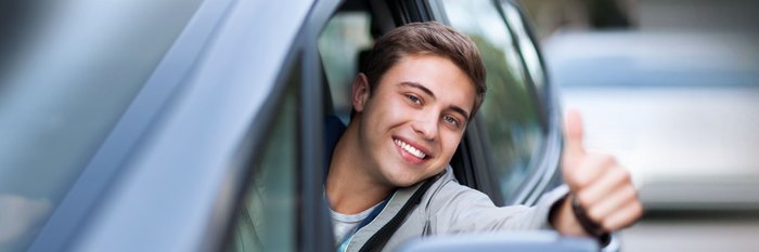 Junger Mann ragt sich aus dem Autofenster und zeigt Daumen hoch.