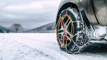 Autoreifen in Schneeketten auf verschneiter Straße.