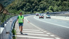 Mann mit Warnweste läuft auf dem Seitenstreifen einer Straße entlang. 