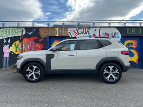 Blick auf die Fahrerseite des Dacia Duster vor einer bunt bemalten Wand
