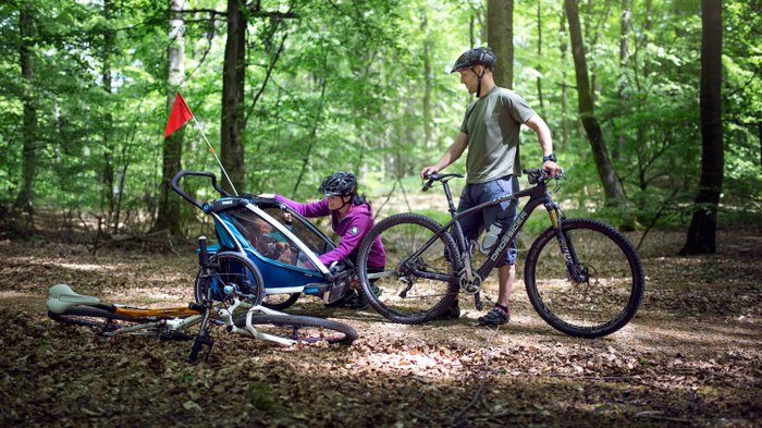 Ein Fahrrad mit Fahrradanhänger von Thule auf einem Waldweg.
