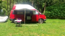 Roter T4 Camper auf einer Wiese, bereit zum Urlaub machen.