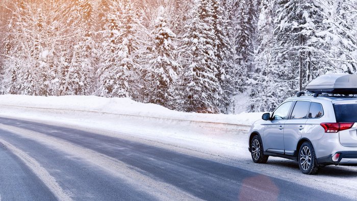 Auto mit Dachbox fährt durch verschneite Winterlandschaft. 
