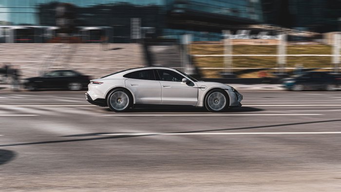 Ein grauer Porsche Taycan Turbo S fährt auf einer Straße durch die Stadt.