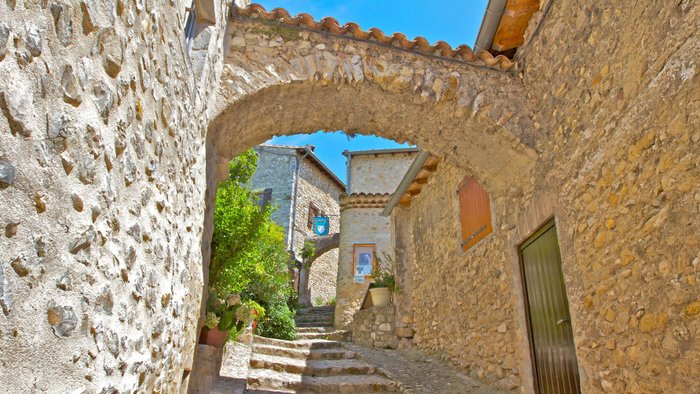 Verwinkelte Dorfgasse mit Steinhäusern, Torbögen und Pflanzen.