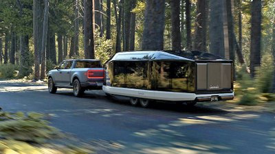 Lightship-Caravan wird auf einer Straße im Wald von einem Pick-up gezogen.