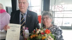 Mann mit ARCD-Treueurkunde in der Hand, daneben Frau mit Blumenstrauß.