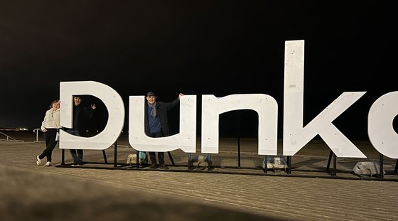 Personen stehen vor den großen Buchstaben von Dunkerque am Strand.