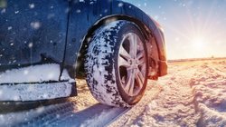 Vorderachse eines Autos mit Winterreifen auf schneebedeckter Straße bei Sonnenschein.