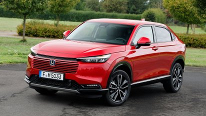 Der Honda HR-V 2025 steht auf Asphalt vor einer Parkanlage.