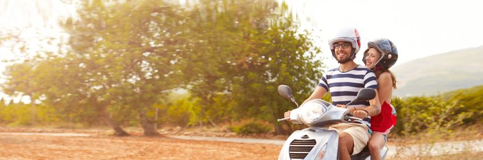 Junges Paar fährt auf Motorroller durch sonnige Landschaft.