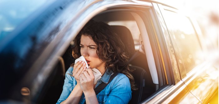 Frau sitzt im Auto und putzt sich die Nase. 