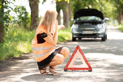 Frau kniet vor einem Auto. 