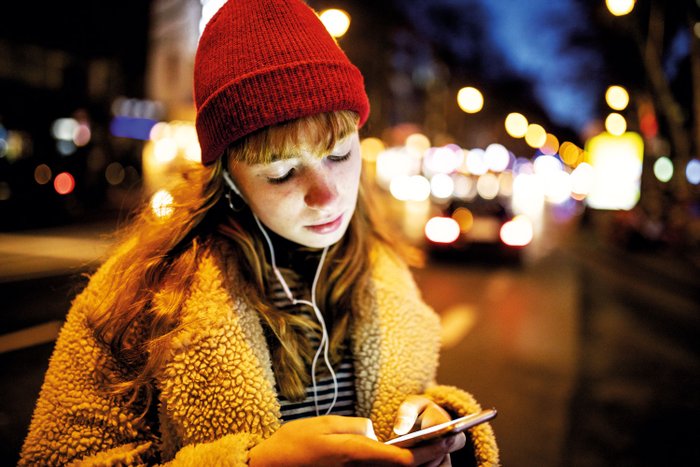 Eine Fußgängerin ist nachts mit dem Smartphone im Straßenverkehr unterwegs. 