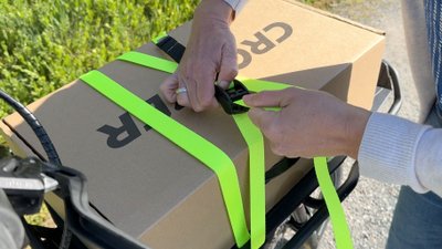 Ein Paket ist mit einem Verzurrgurt auf dem Lastenrad befestigt. 