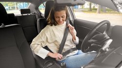 Eine junge Frau sitzt im Auto und schnallt sich an.  