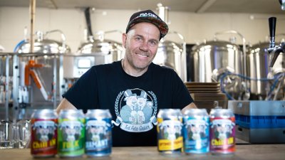 Mann mit Basecap und T-Shirt steht hinter bunten Bierdosen an einem Tresen.