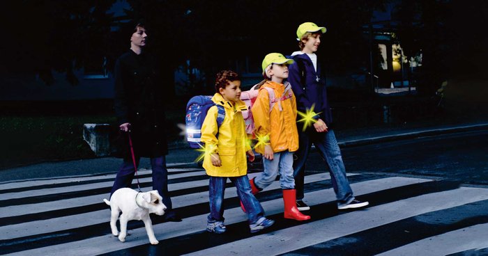 Kinder laufen mit reflektierende Kleidung in der Nacht auf einer Straße.