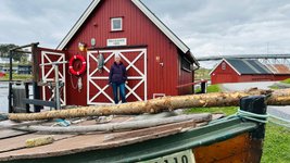 Rote Holzhäuser in skandinavischem Stil und ein Boot an einem Flussufer.