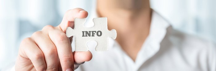 Nahaufnahme einer Hand, die ein Puzzleteil hält, auf dem das Wort Info aufgedruckt ist.