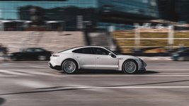 Ein grauer Porsche Taycan Turbo S fährt auf einer Straße durch die Stadt.