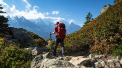 Mann mit Rucksack wandert auf Gebirgspfad; schneebedeckte Gipfel am Horizont.