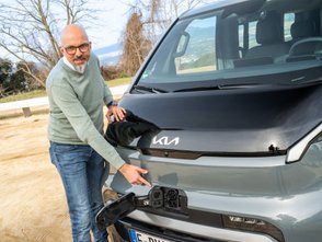Ein Mann zeigt auf den Ladeanschluss des Kia PV5. 